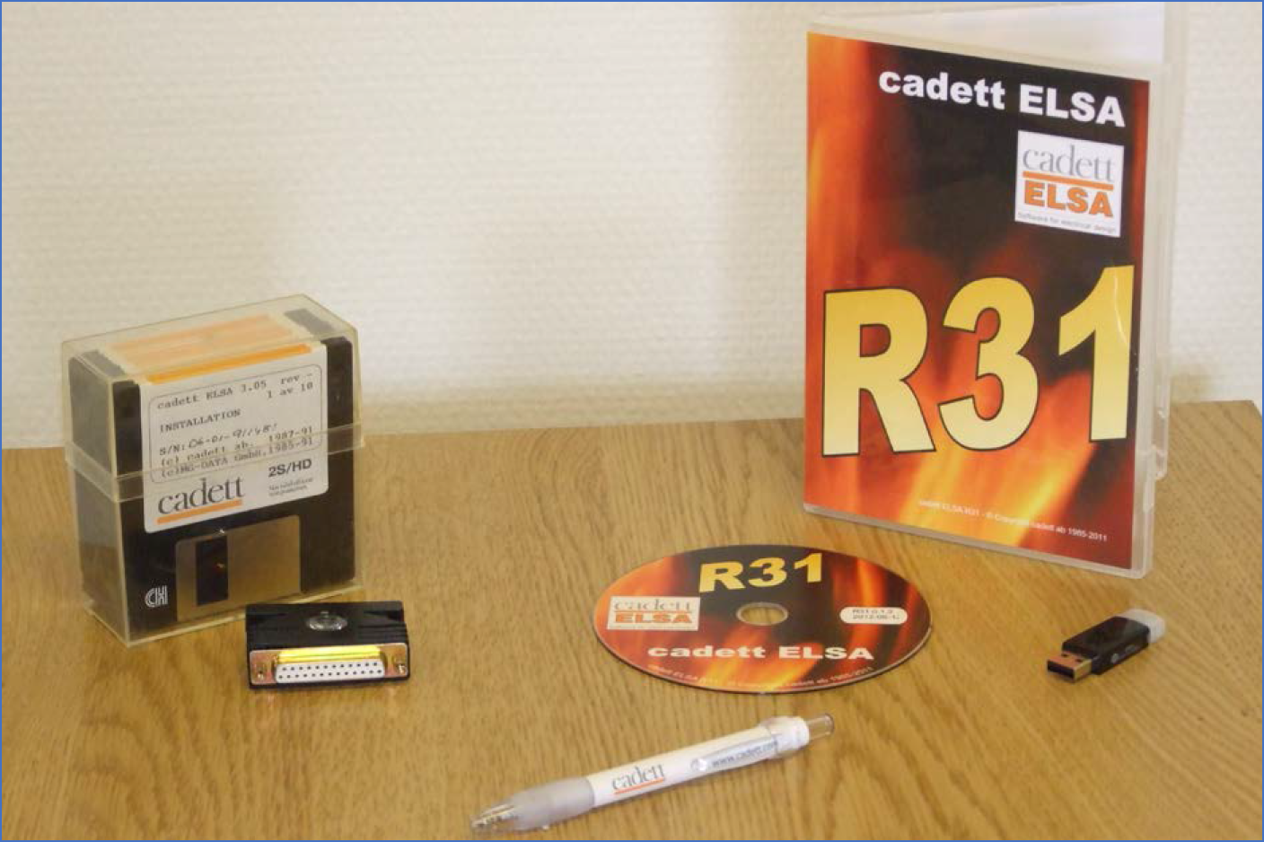 Figure 2309: &nbsp;This figure shows legacy installation packages. To the left, cadett ELSA 3.05 from 1991 with 10 diskettes and a parallel port hardware lock. To the right, cadett ELSA R31 from 2011 with a DVD and a USB port hardware lock. 20 years had passed between them. In 2026, yet another 15 years later, physical media is no longer in use. The software is downloaded as one single executable file from the internet.